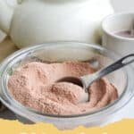 Cozy Comfort in a Cup: The Best Easy Homemade Hot Cocoa Mix Recipe 6 A close-up of a glass jar filled with homemade hot cocoa mix, with a wooden scoop beside it and a cozy mug of prepared hot cocoa in the background.