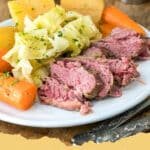 A large plate of sliced corned beef with tender cabbage wedges, carrots, and potatoes, ready to be served.