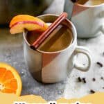 A steaming mug of traditional Wassail garnished with orange slices and cinnamon sticks on a festive table.