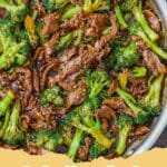 A close-up shot of a vibrant Beef and Broccoli Stir-Fry in a white bowl, garnished with sesame seeds, with chopsticks resting on the side.