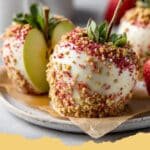 Close-up of vibrant red Strawberry Shortcake Candy Apples with a crumbly topping on wooden sticks, arranged on a rustic wooden board.